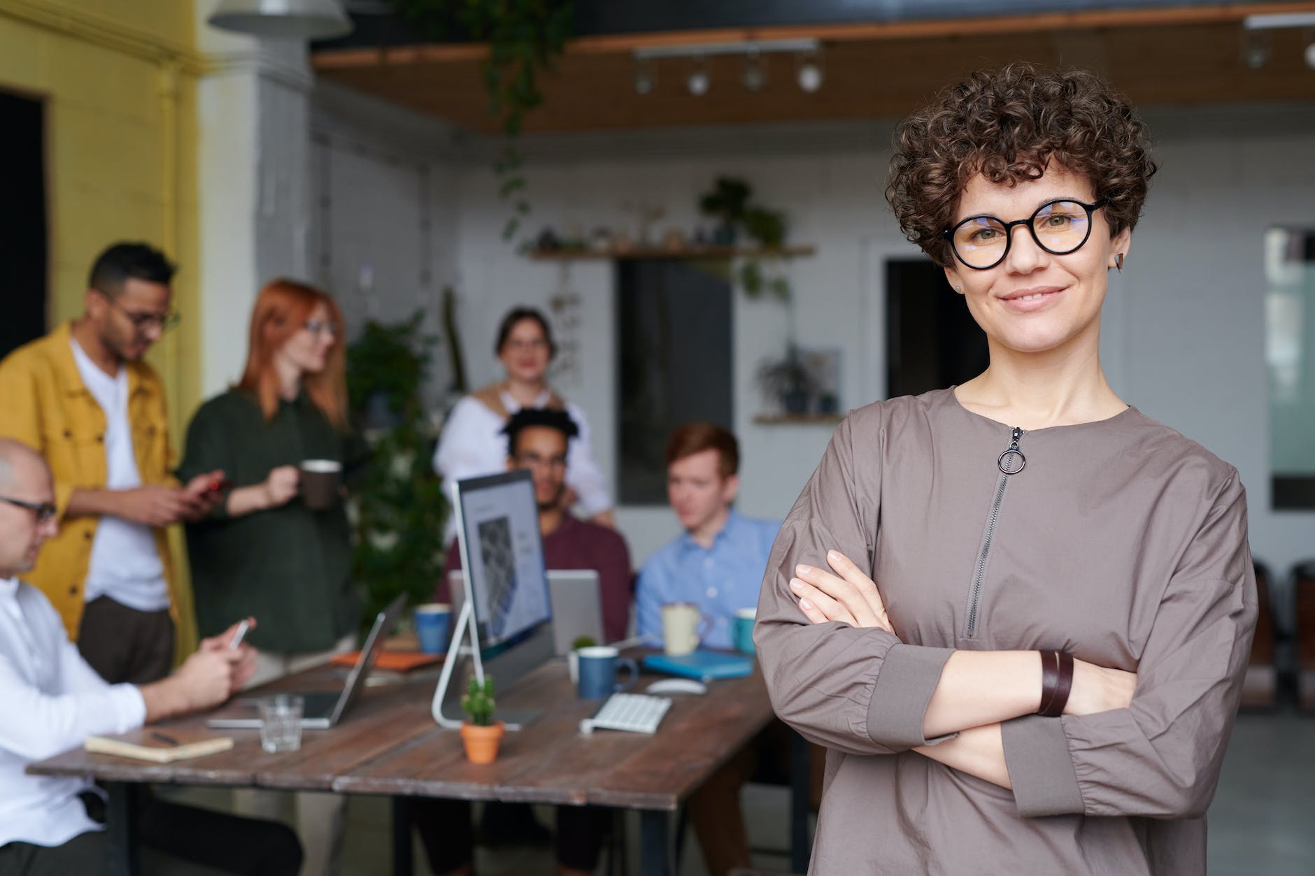 a picture of a woman smiling, with her co workers in the background attending a meeting
